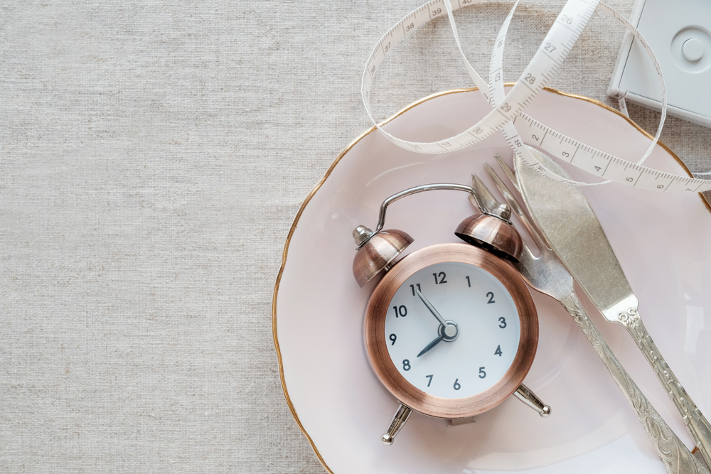 Intermittent fasting depicted by clock on plate and tape measure Intermittent fasting depicted by clock on plate and tape measure