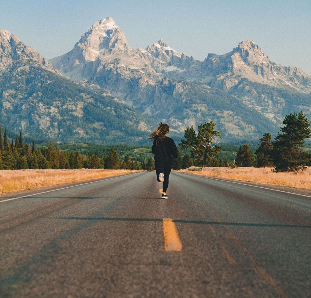 woman running down road toward mountains woman running down road toward mountains