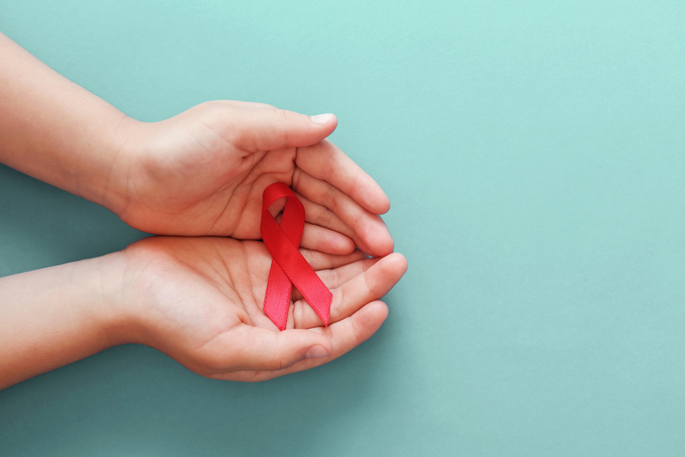 Hands holding red ribbon on blue background, hiv awareness Hands holding red ribbon on blue background, hiv awareness