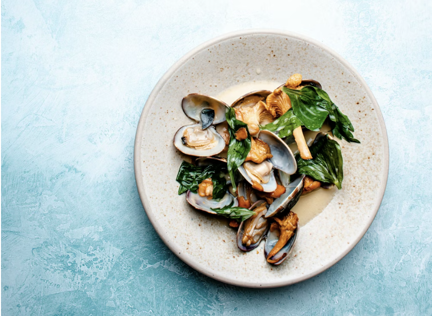 shellfish and greens plated on blue background