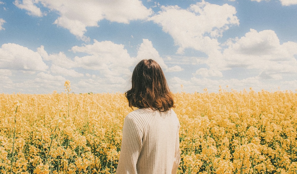 woman facing blooming field and sky