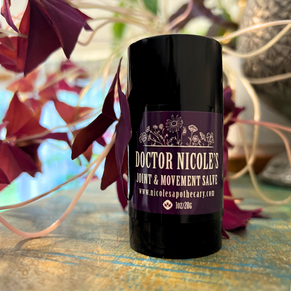 Nicole's Apothecary Joint & Movement Salve Stick with purple shamrocks on green wood shelf